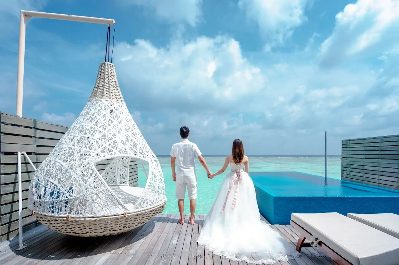 Home A newlywed couple holding hands, enjoying a seaside resort with infinity pool.