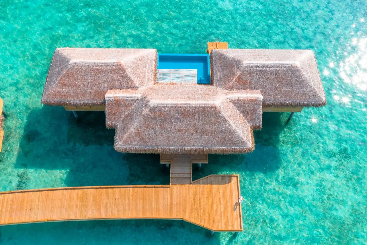 Home Stunning aerial view of an overwater villa in a clear turquoise lagoon in the Maldives.