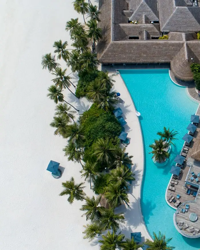 Contact Aerial drone shot of exotic resort with empty hotel territory with green palms and blue swimming pool with sunbeds in sunlight